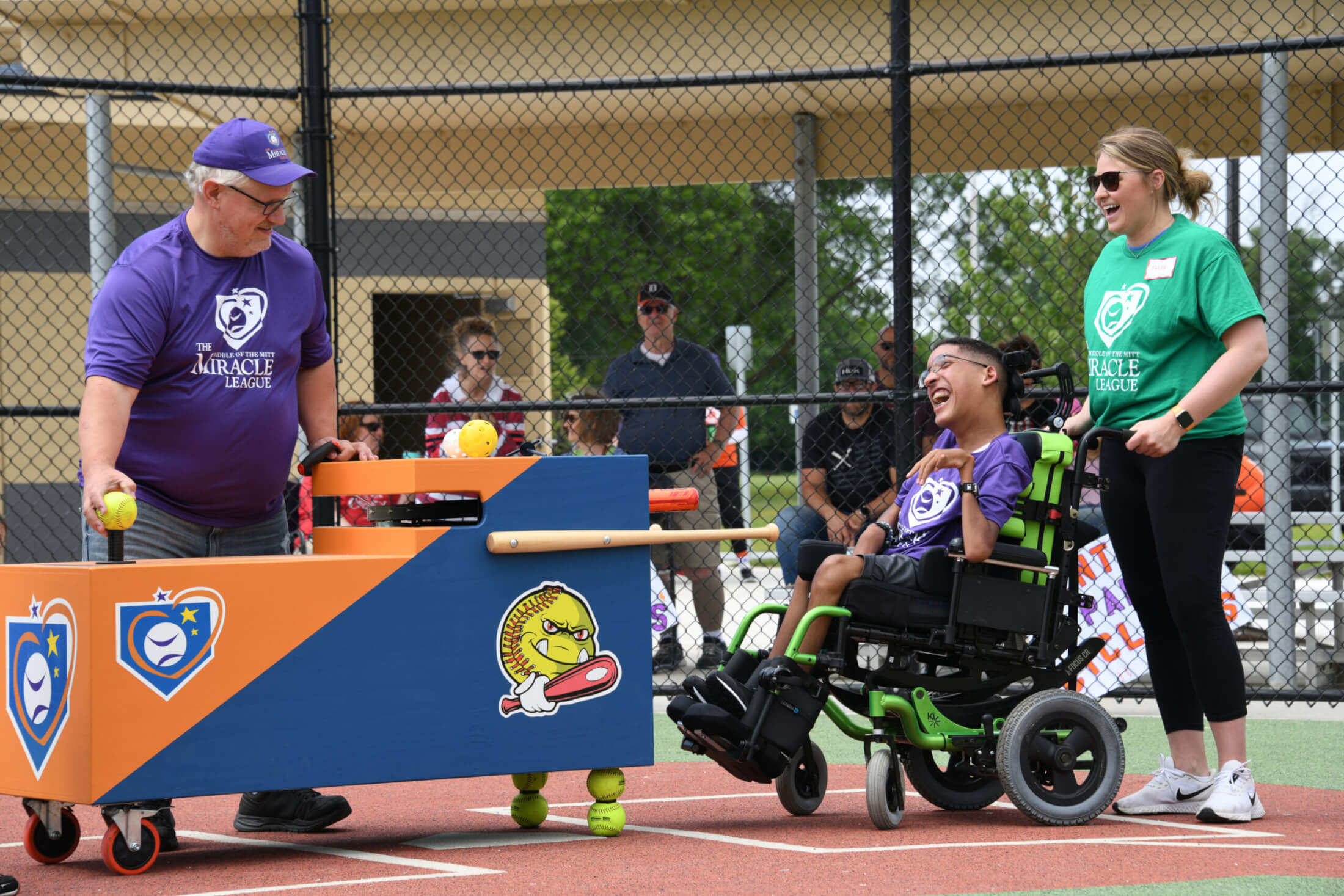 Photo of a young man in a wheelchair participating in The Miracle League baseball program in Midland, Michigan, with volunteers.